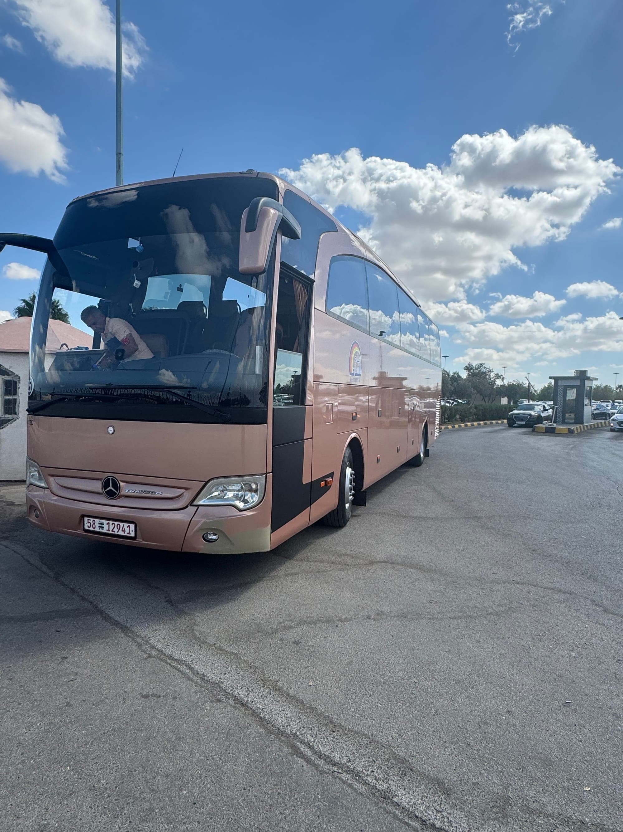 A rose-gold Belad Al Sham Mercedes-Benz Travego coach, parked under a blue sky
